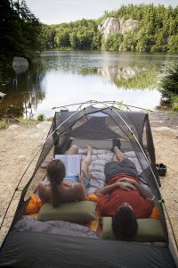 Couple lounges in open tent near lake