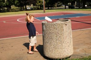 Little boy throws carton into trashcan in park